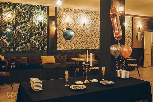 Sala Aqua Hostel en Barcelona con papel pintado botánico, apliques dorados, mesa montada con copas de cava y globos para una celebración
