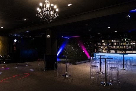 Sala Black en Barcelona, salón lounge oscuro con lámpara de araña, barra iluminada con taburetes transparentes y luces de fiesta
