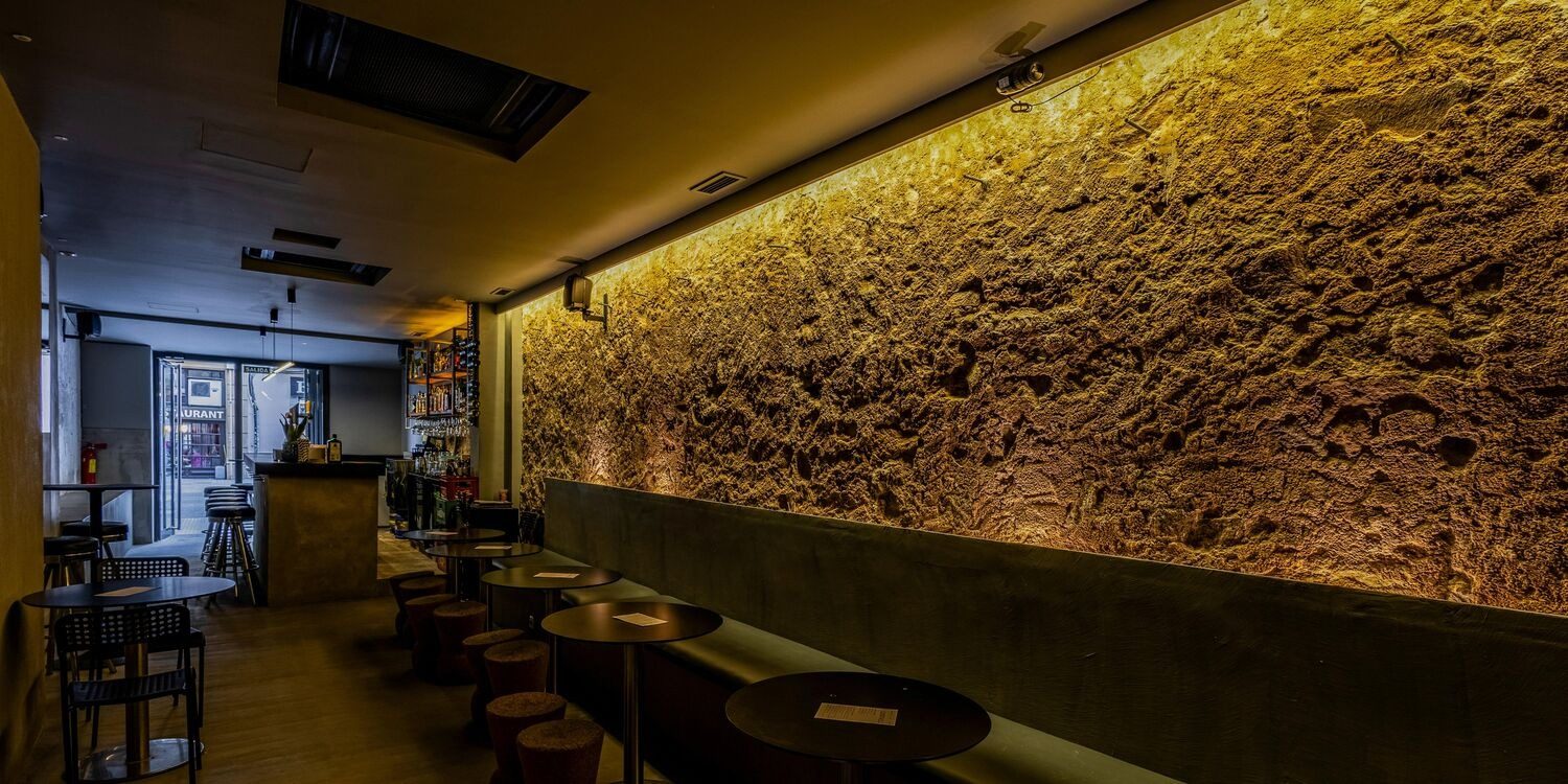 Sala Quinto en Barcelona, espacio rústico con pared de piedra iluminada y mesas altas